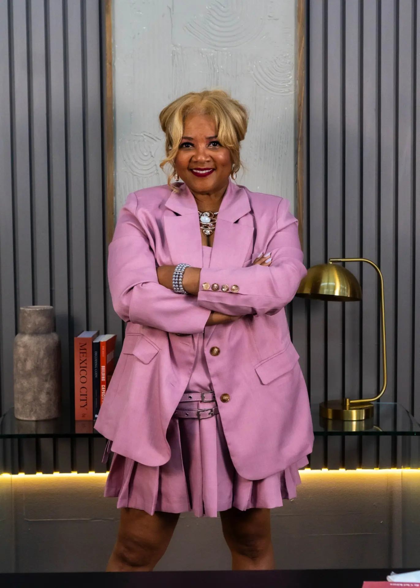 Kitura Smith standing with arms crossed in a pink suit, confident and approachable